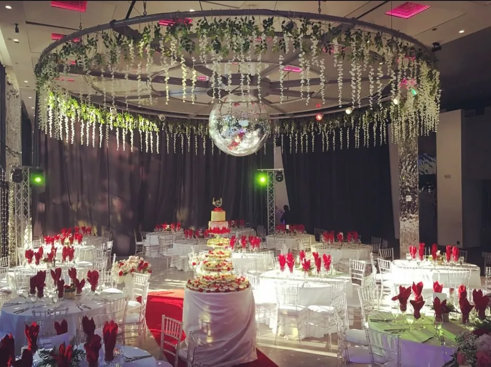 Hall set with red napkins and a tiered cake under a floral chandelier
