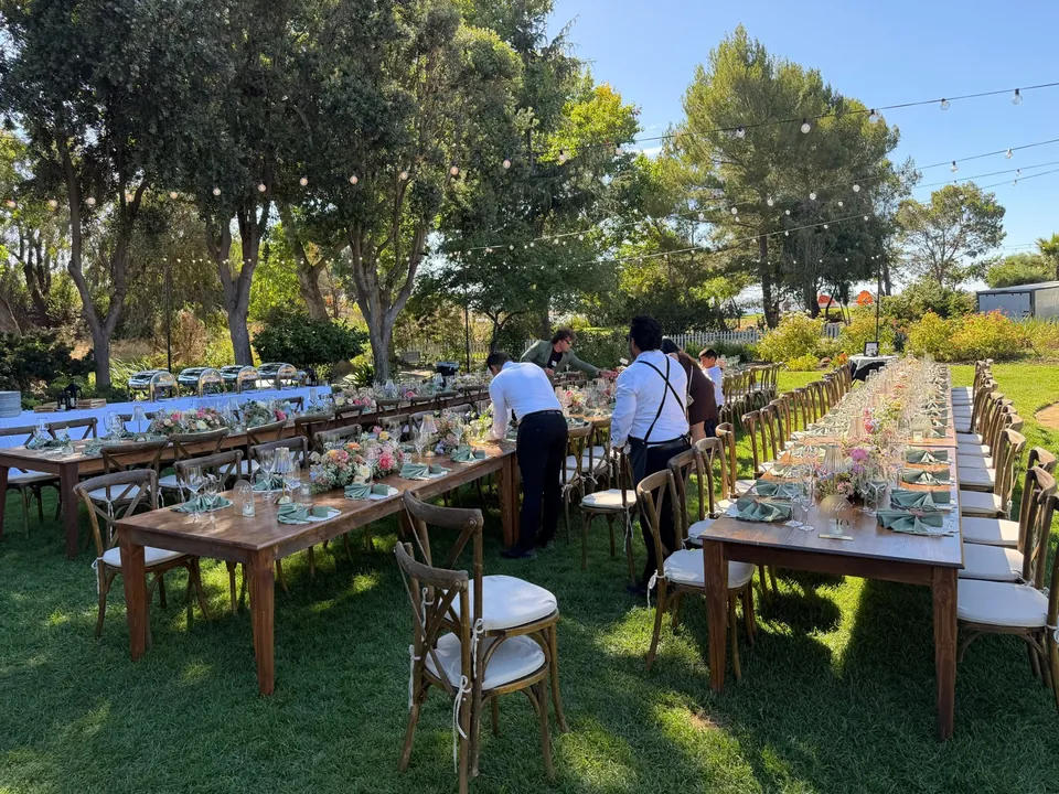 Caterman staff setting long wooden tables on a lawn before guests arrive