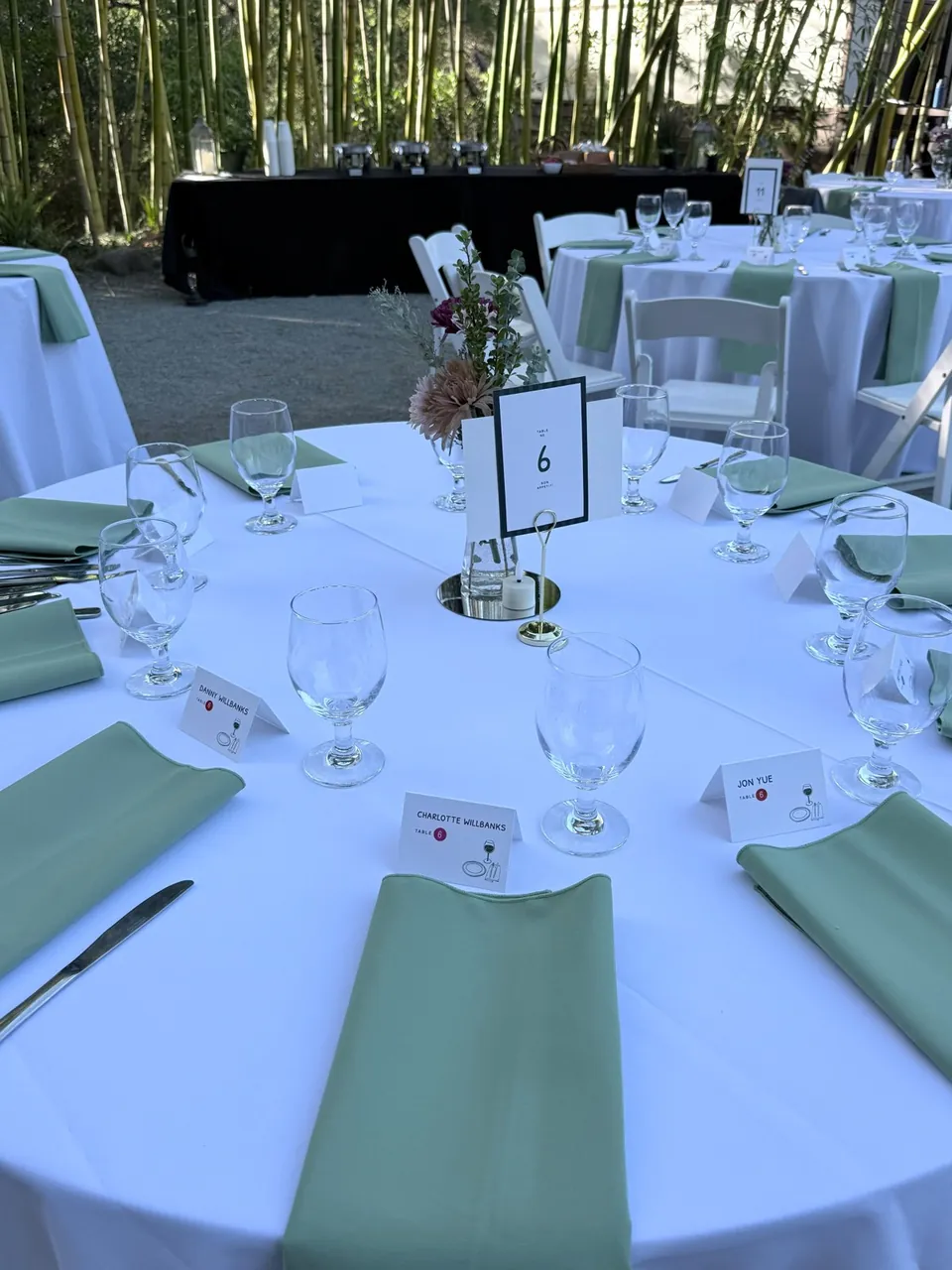 Round tables with white cloths and sage green napkins in a bamboo garden