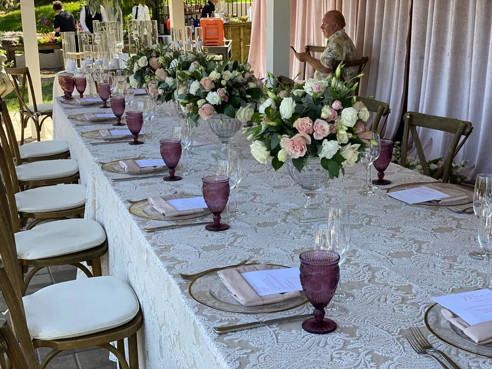 Long table under a tent with lace linen, plum glassware and pink roses