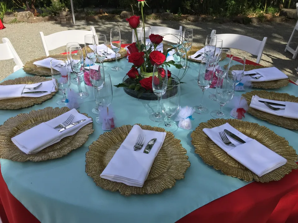 Round table with turquoise cloth, gold chargers and red roses