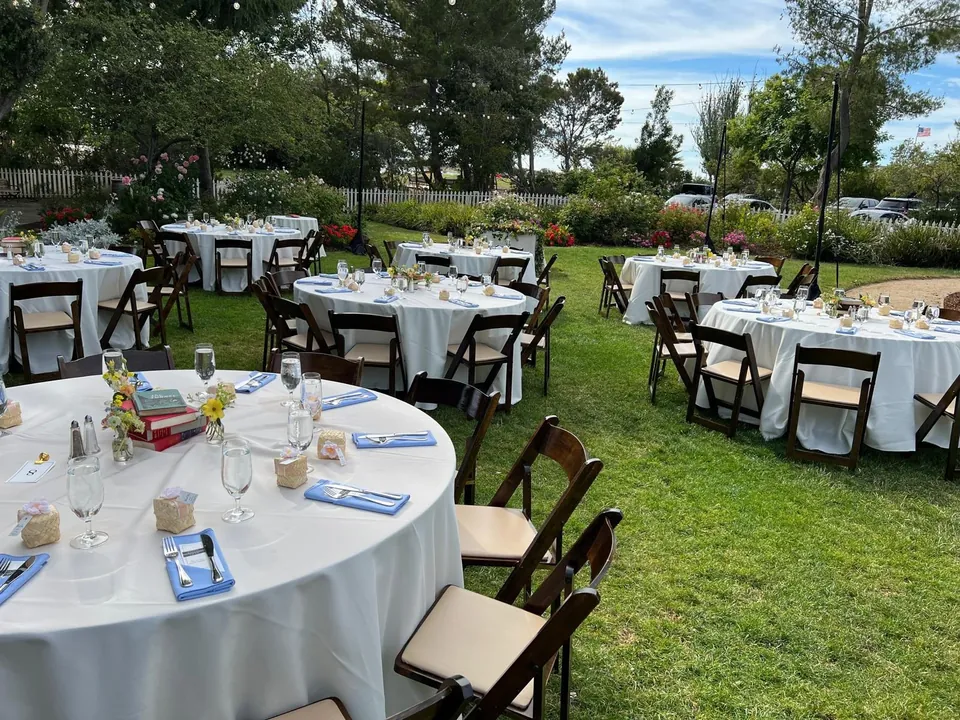 Round tables set on a lawn with white linen and wooden chairs